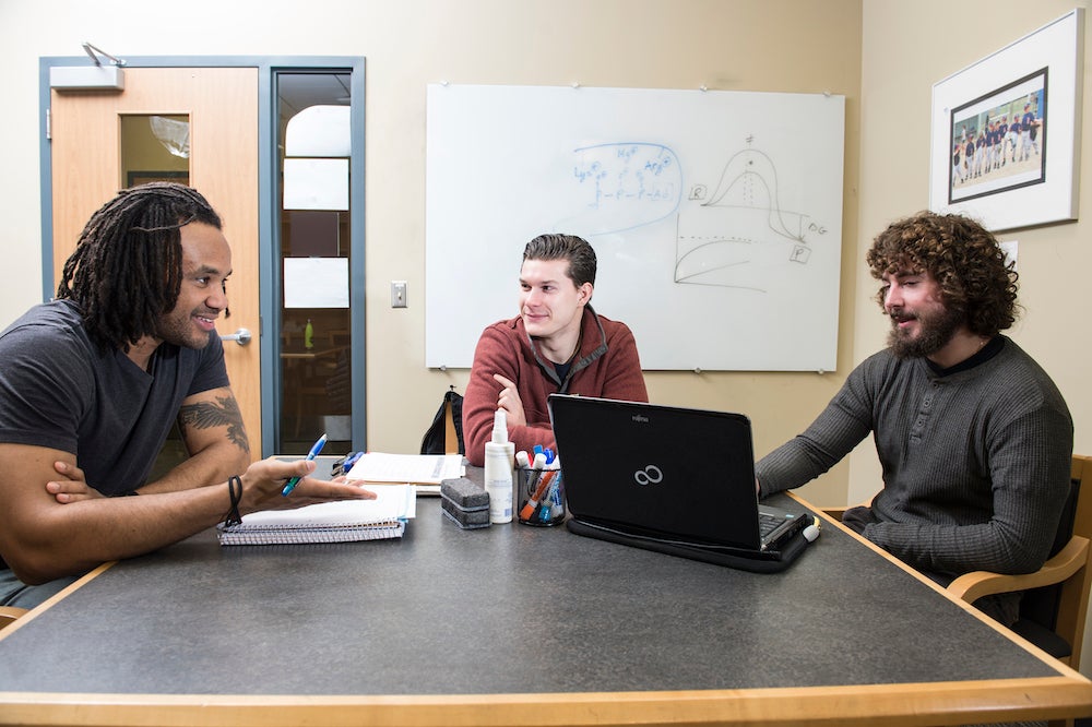 three students sit around a table in conversation with each other.