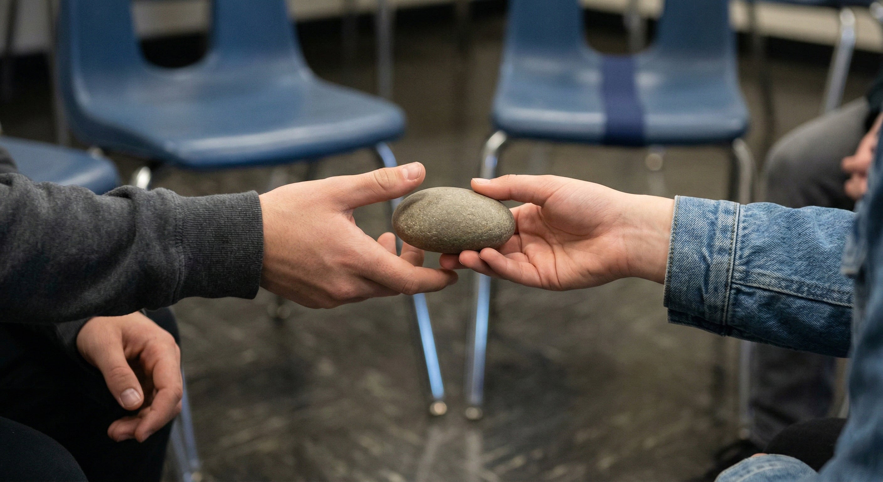 Hands passing a smooth stone in a circle of chairs