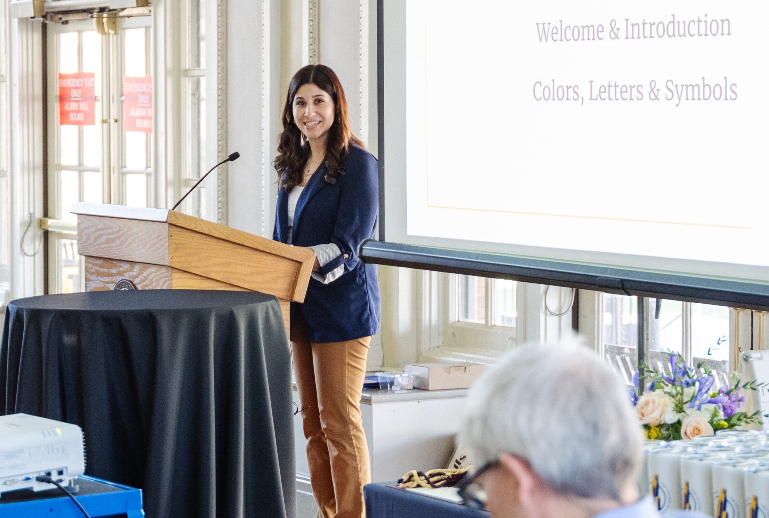 person standing at podium, smiling at audience.