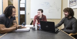 three students talk with each other around a table.