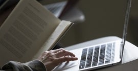 Student holds text book while using a computer