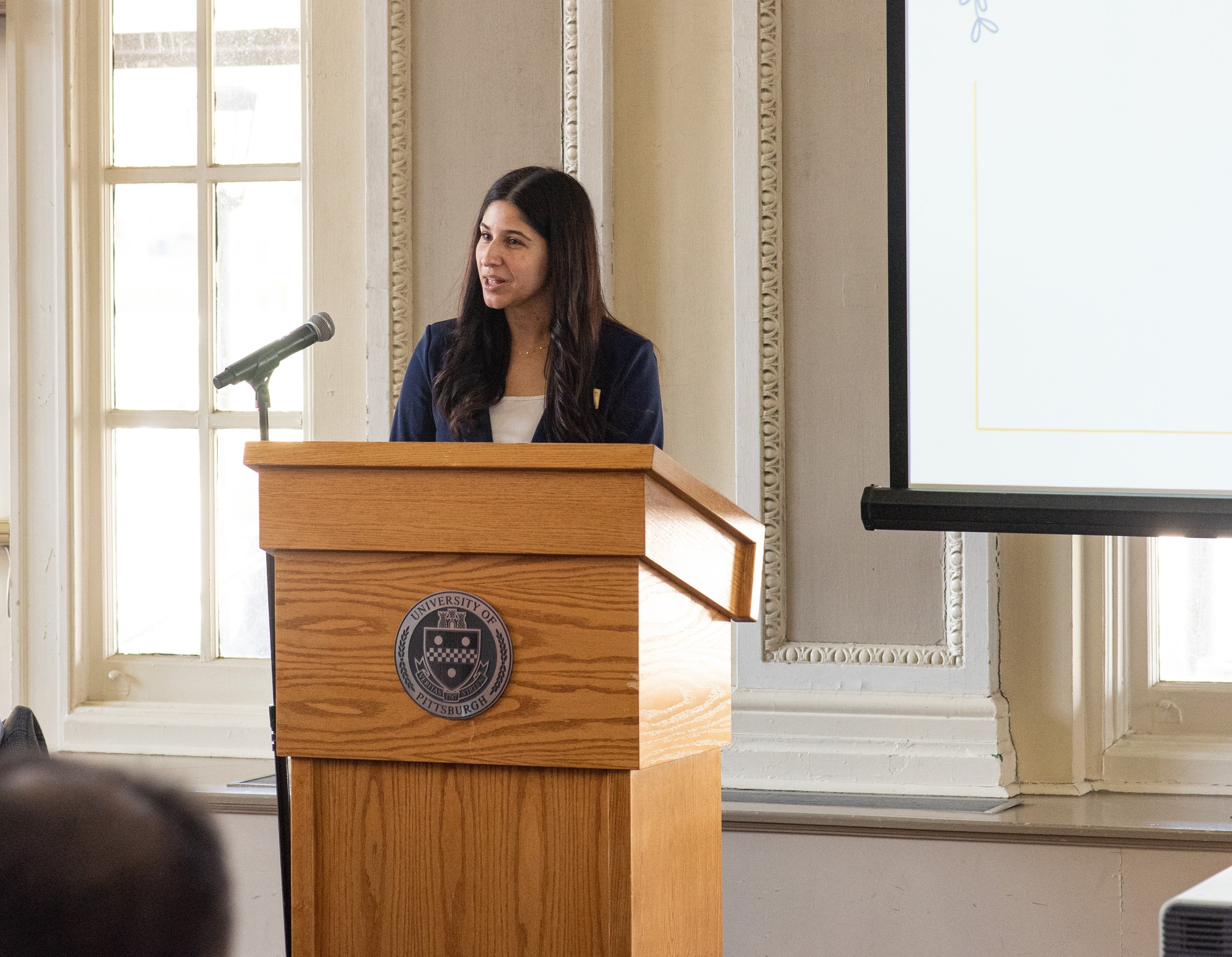 person standing at podium, smiling at audience.