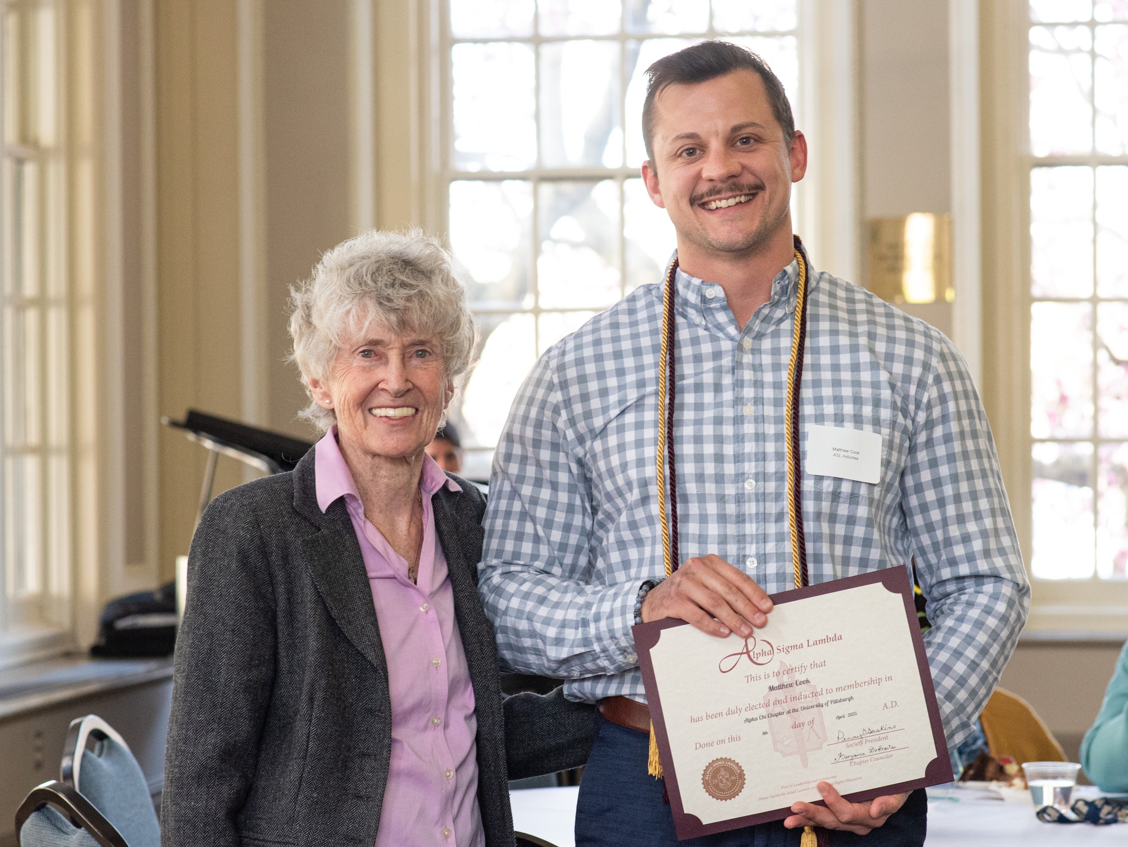 three people standing, one holding a certificate and wearing a cord. 