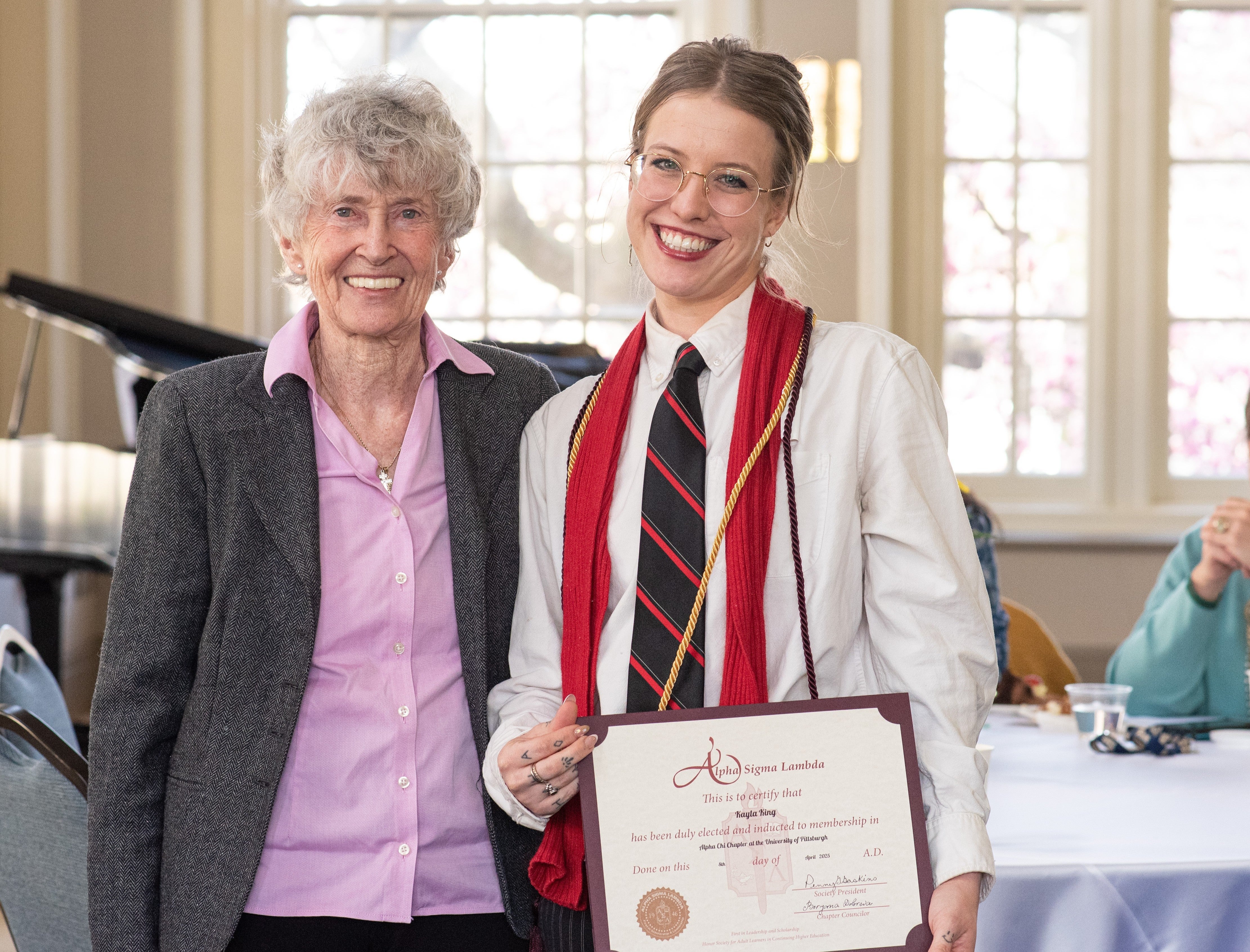 three people standing, one holding a certificate and wearing a cord. 
